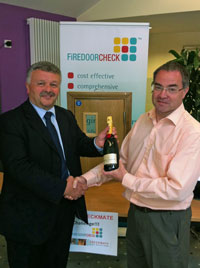 Steve Wiggins - University of Bradford Fire Safety Officer receives the prize of a bottle of Champagne from Clive Reilly of Checkmate Fire Solutions